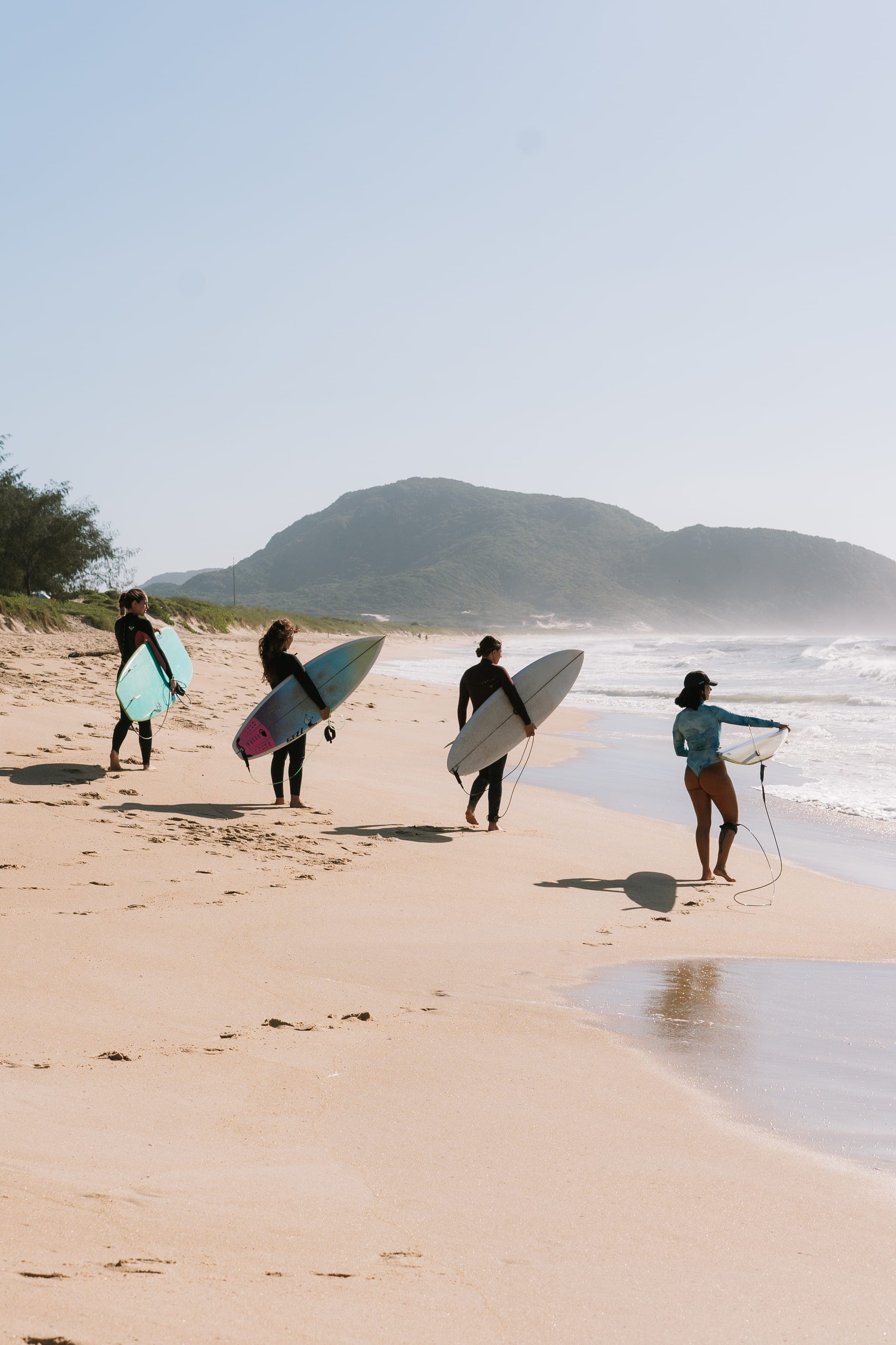 Four women carrying surfboards along the beach toward the water.