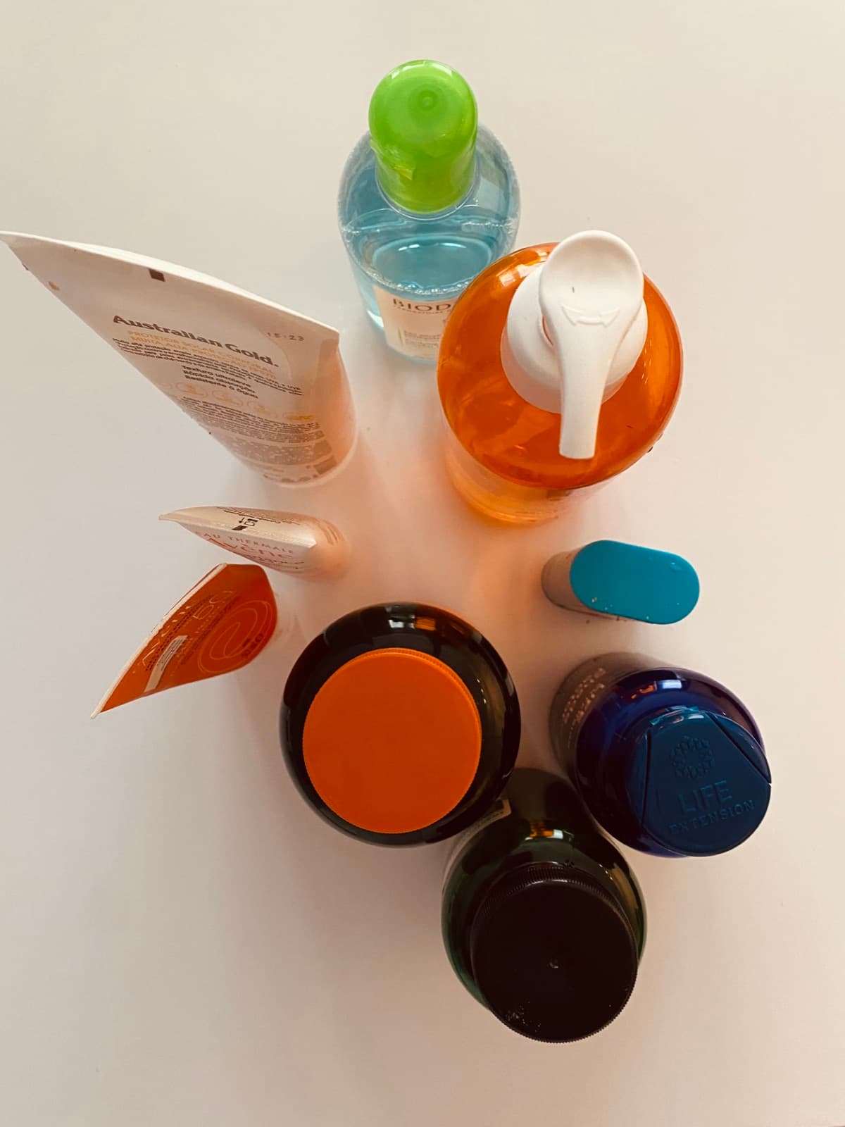 Skincare products seen from above on a white table: micellar water, face wash, moisturisers, a sunscreen stick and a lip balm.