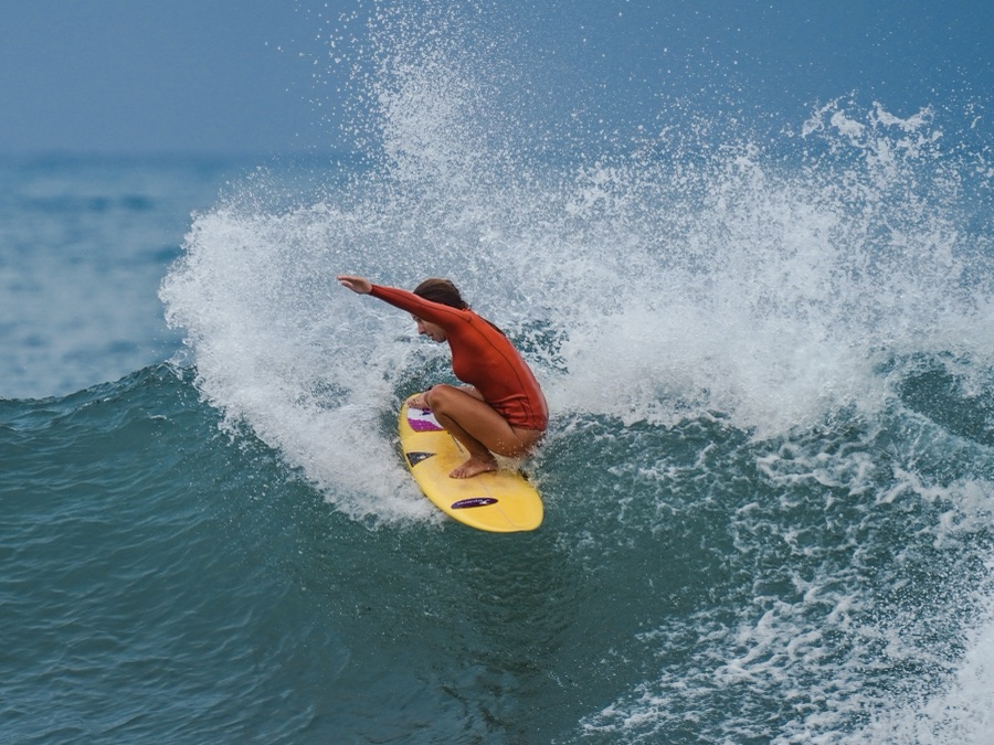 A surfer in an orange rash guard carving a turn off the top of a wave on a yellow board